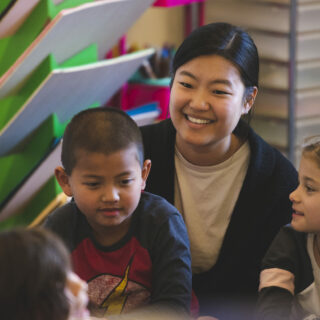 Student teacher sitting with two young students in a classroom