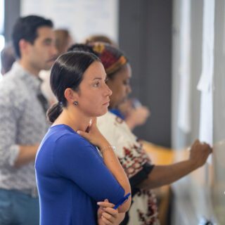 A student stands in front of a white board thinking about what to write