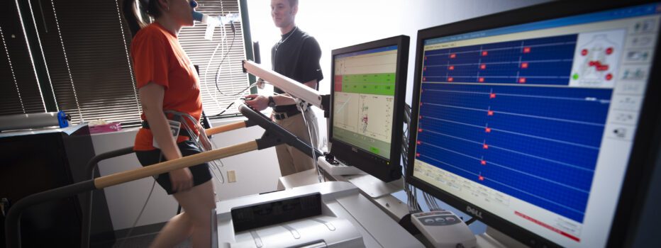A student walking on a treadmill hooked up to a machine measuring her rate rate and breathing