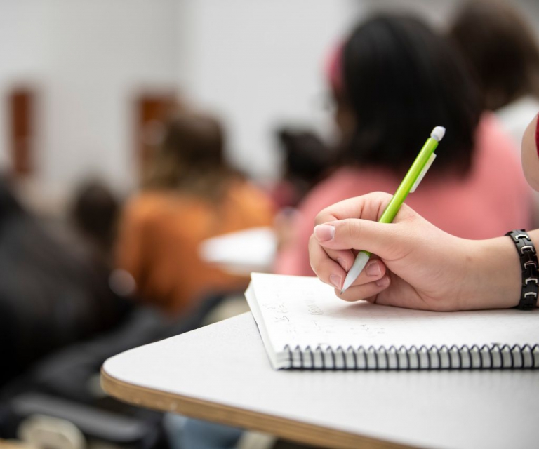 A person with a pencil writing on paper in a classroom