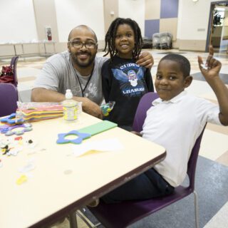 A teacher is joined by two young students in a city school and they are smiling