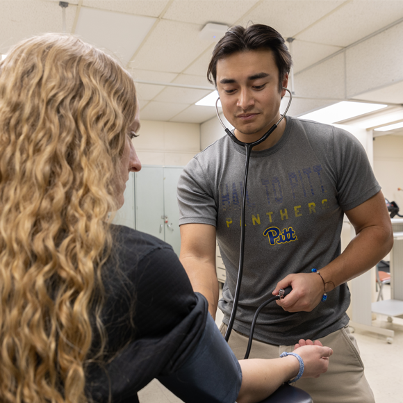 A student performing a blood pressure test on another student in a classroom