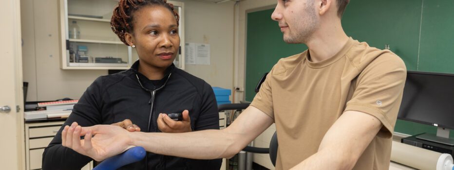 A student takes the pulse of another student on a stationary bike.