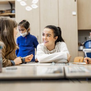 Student teacher crouches by the desk of a young student