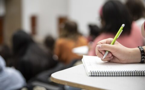 Hand taking notes on paper in classroom