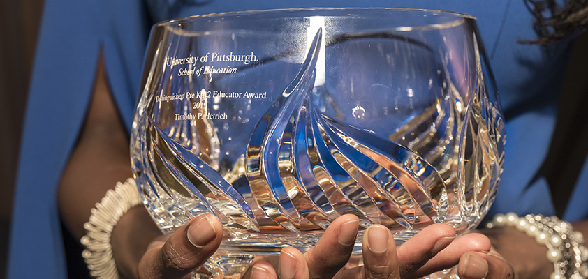 Close-up of someone holding a glass Alumni Award trophy