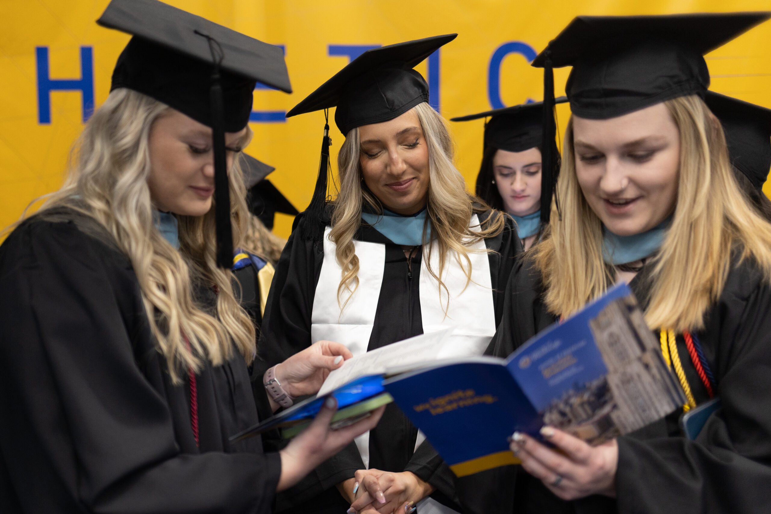 Three students in graduation regalia look through a program