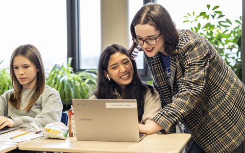 Student-teacher helps a young student on a laptop