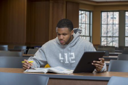 A male black student wearing a 412 pittsburgh shirt reading and studying