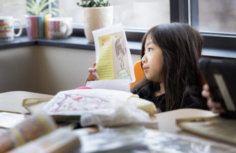 A young girl sitting in a classroom reading a paper