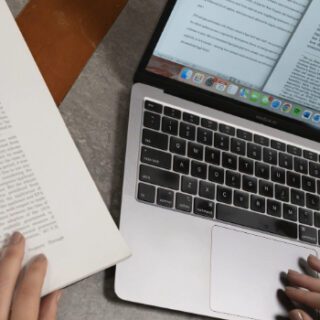 Hands typing on a keyboard in front of a laptop next to a math book