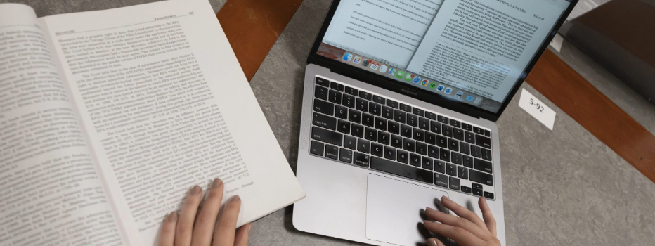 Hands typing on a keyboard in front of a laptop next to a math book