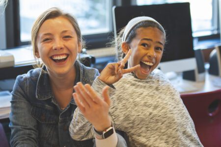 A student teacher with a student, both smiling and holding up their hands