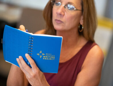A teacher holding a book that says Western PA Writing Project on it