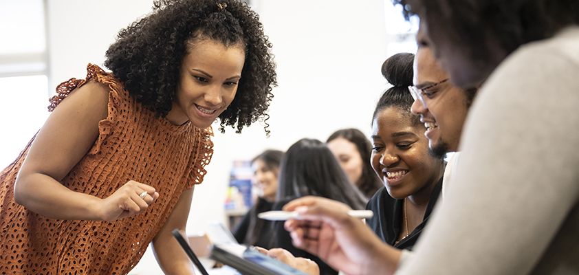 A person leans over a group of students working on tablets