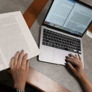 Hands working on a laptop and turning a page in a book