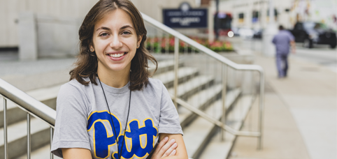 Student in Pitt shirt standing outside Pitt's campus