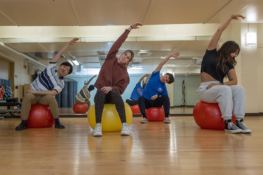 http://Four%20students%20do%20a%20side-stretch%20while%20sitting%20on%20stability%20balls