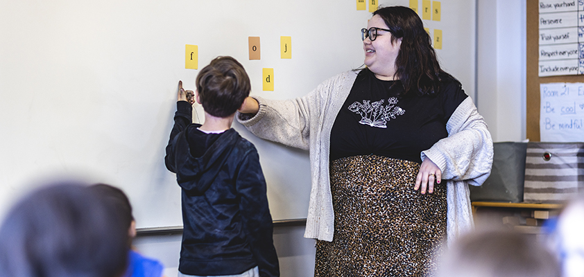 Student teacher and an elementary student point to letters on a whiteboard