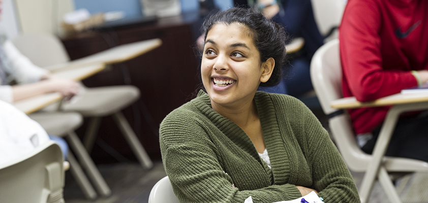 Student smiling while sitting at a classroom desk