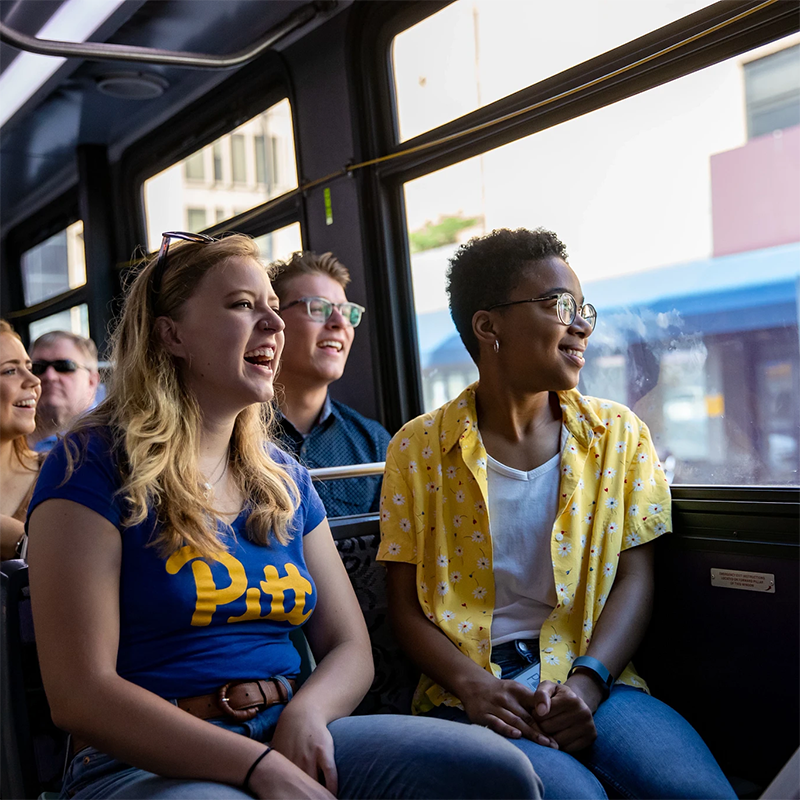 Pitt students sitting on a bus and looking out the window draggable=