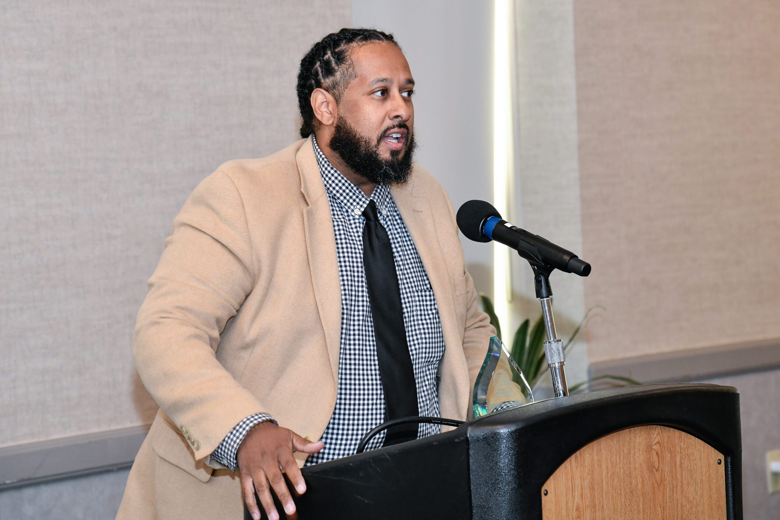 Stephen Walker, wearing a light brown blazer and a gray shirt underneath, speaks at a podium while accepting the Keepers of the Flame Award at the PASSHE Awards Ceremony at Kutztown University.