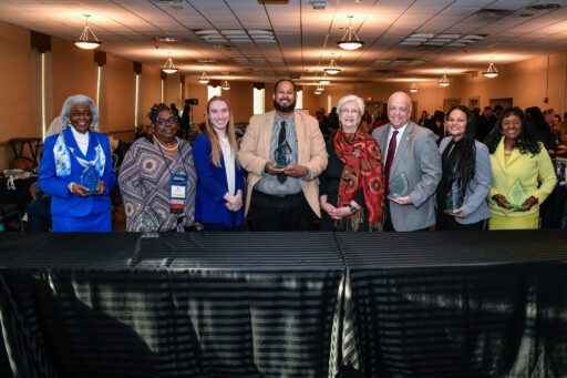 Stephen Walker, Center, wearing a light brown blazer and a gray shirt underneath, poses with seven other individuals during the PASSHE Awards Ceremony at Kutztown University