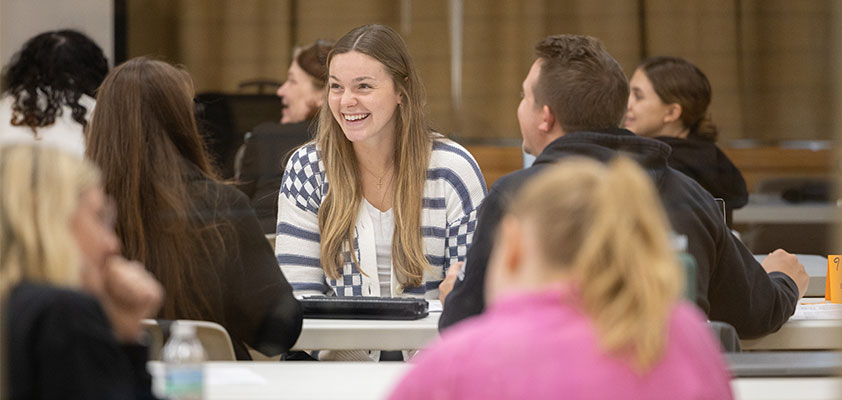 A student smiling in a classroom with her classmates at Pitt