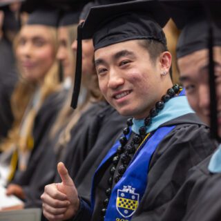 Male student giving thumbs up sign at school commencement ceremony
