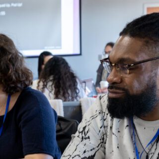 A man and a woman learning together in a classroom, sitting at a table with a backpack and drinks