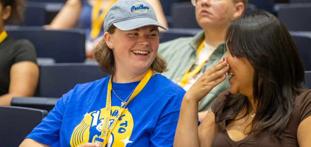 Two girls talking at new student orientation in a crowded auditorium room